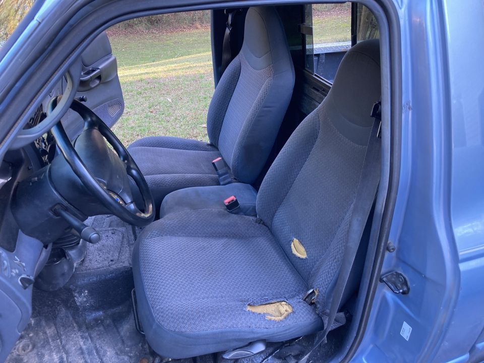 Interior of a blue Ford Ranger pickup truck showing the driver's seat and steering wheel with ripped upholstery.