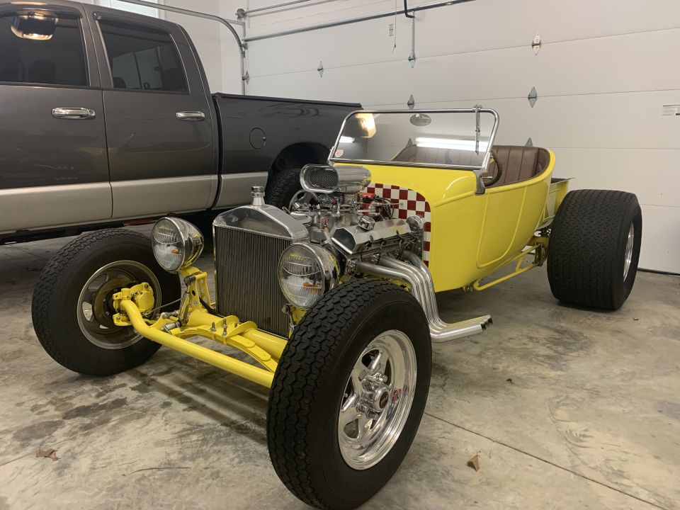 Yellow 1923 Ford Model T hot rod with chrome engine and checkered decal parked in garage.