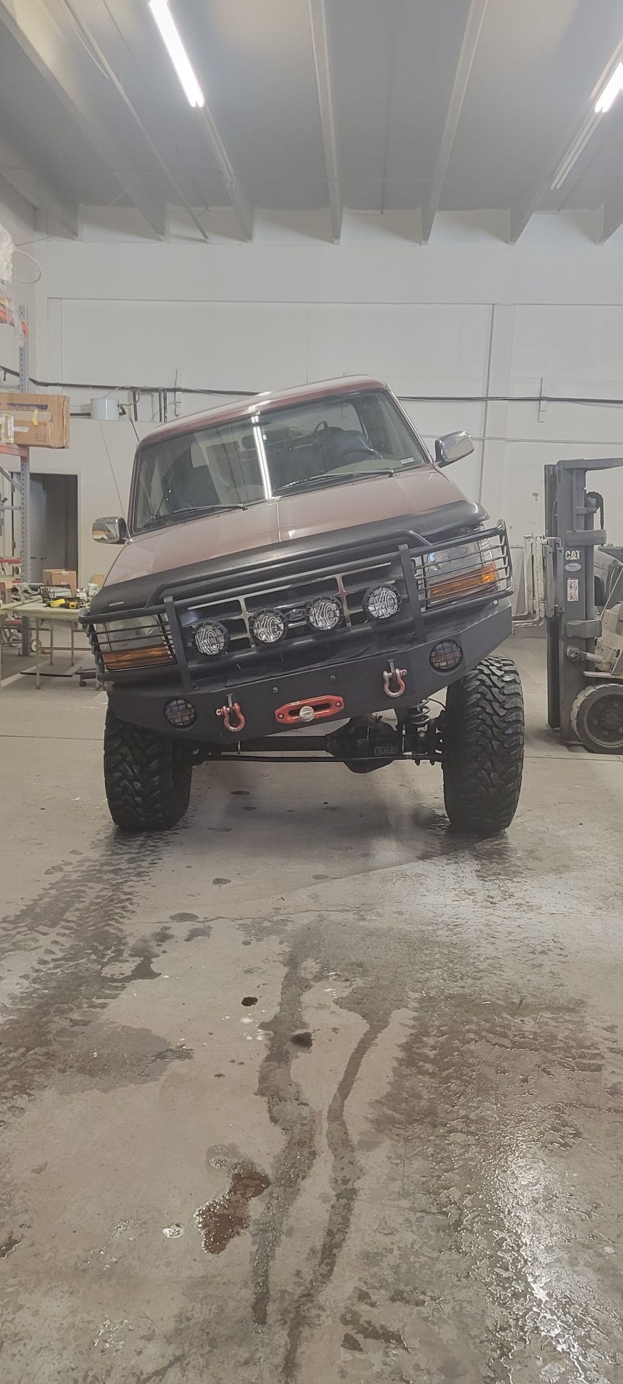 1996 Ford Bronco with aftermarket bumper and KC lights, tilted on wet floor.