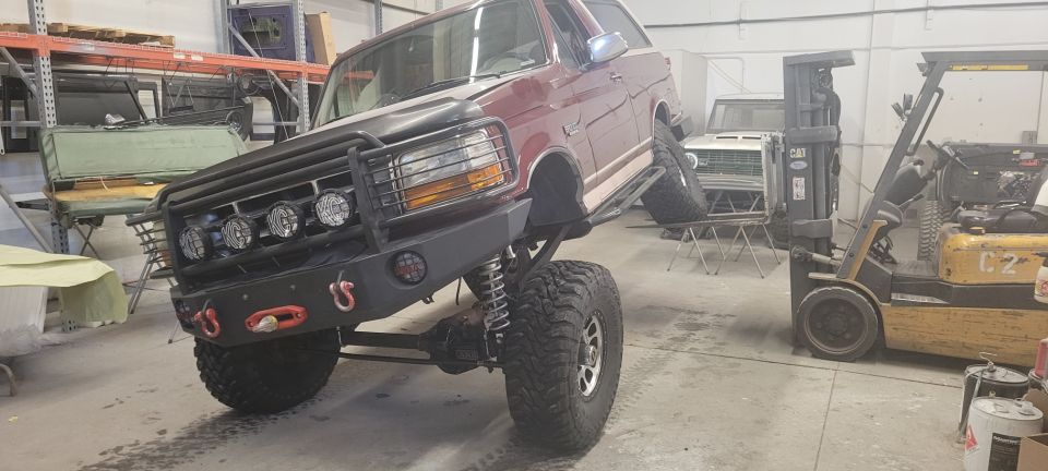 Lifted 1996 Ford Bronco with custom bumper and lights, parked indoors next to a forklift.