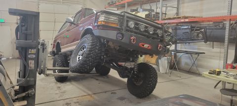 1996 Ford Bronco - A lifted burgundy 1996 Ford Bronco is being held up by a forklift in a workshop. The vehicle has a custom front bumper with a winch and aux…