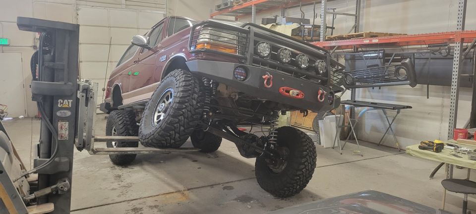 Lifted 1996 Ford Bronco with custom bumper and lights on a forklift in a workshop.