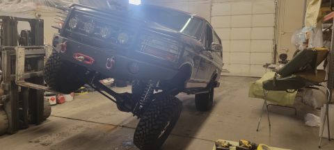1996 Ford Bronco - A heavily modified dark-colored SUV, possibly a Ford Bronco, is lifted by a forklift in what appears to be a garage or workshop. The vehicl…