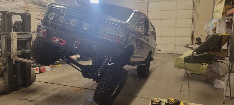 Modified dark SUV on forklift with off-road tires and custom bumper.