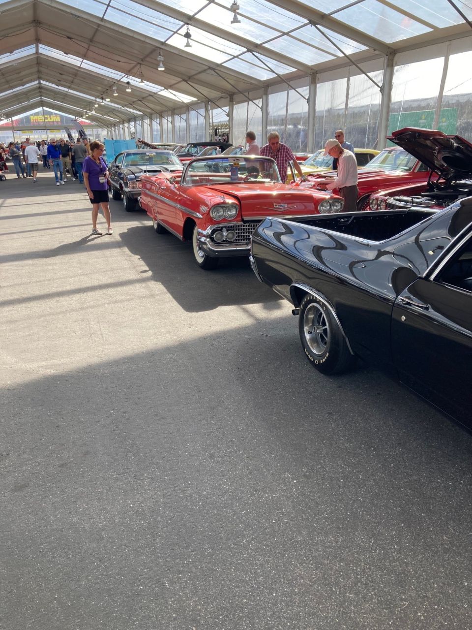 Classic cars displayed under a tent, featuring a red convertible and a black coupe.