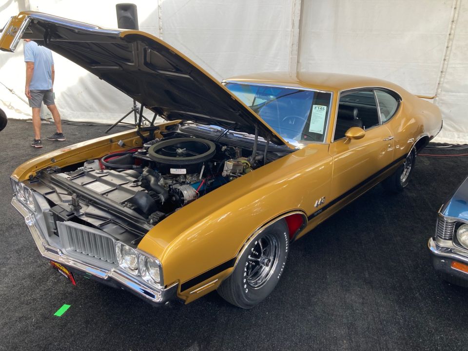 Gold 1969 Oldsmobile 442 muscle car, hood open, showing engine, black stripe on side, chrome wheels