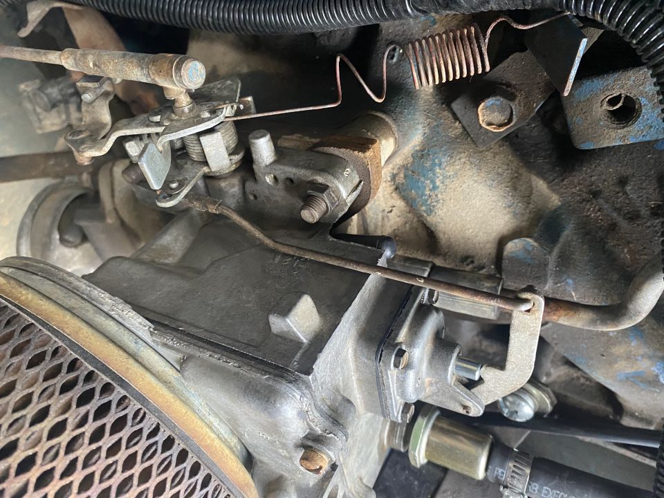 Close-up of engine carburetor, throttle linkage, springs, and air filter housing.