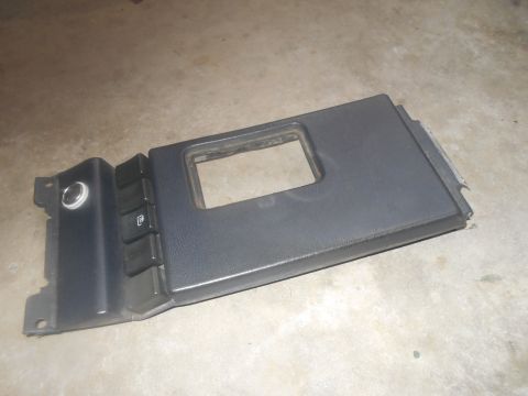 1992 Ford Bronco - A dark gray plastic dashboard trim piece with a rectangular cutout and several buttons is shown on a concrete floor.