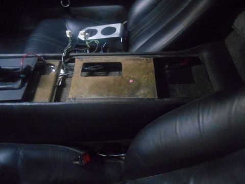 1992 Ford Bronco - The interior of a vehicle shows a disassembled center console with exposed wiring and components. The black leather seats are visible on ei…
