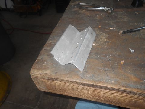 1992 Ford Bronco - A metal bracket with drilled holes sits on a wooden workbench next to a screw and a pair of pliers.