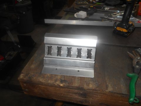 1992 Ford Bronco - A metal bracket with five cutouts sits on a wooden workbench next to a pair of green-handled tin snips and a cordless drill.