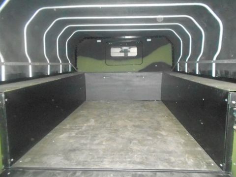 1992 Ford Bronco - The interior of a vehicle bed with black side panels and a camouflage pattern on the rear wall. The ceiling has white, curved support beams.