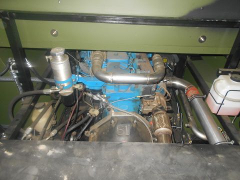 1992 Ford Bronco - A close-up view of the engine bay of a vehicle, showing the blue engine block, silver exhaust pipes, and various hoses and filters. A white…