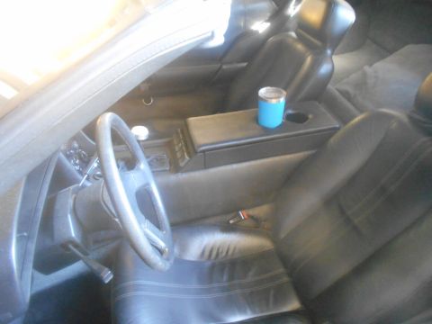 1992 Ford Bronco - The interior of a car is shown, featuring black leather seats, a steering wheel, and a center console with a blue cup. The view is from the…