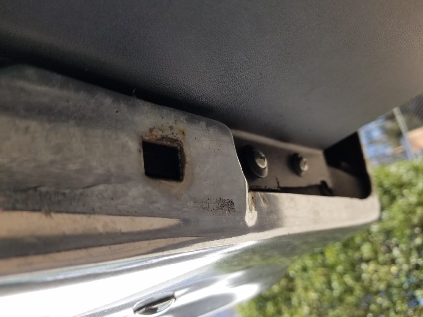 Close-up of a rusty metal bracket with a square hole and bolts on a vehicle.