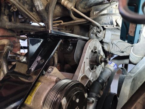 1996 Ford Bronco - A black metal bracket is installed over a Ford engine component, possibly for an accessory. The engine bay is dirty and cluttered with hose…