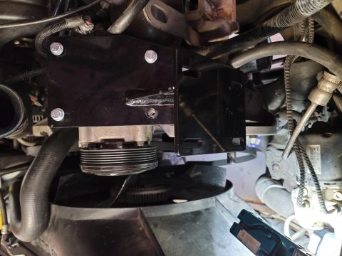 1996 Ford Bronco - A black metal bracket is bolted to the engine of a 1996 Ford Bronco, holding a pulley system. The engine bay is filled with hoses, wires, a…