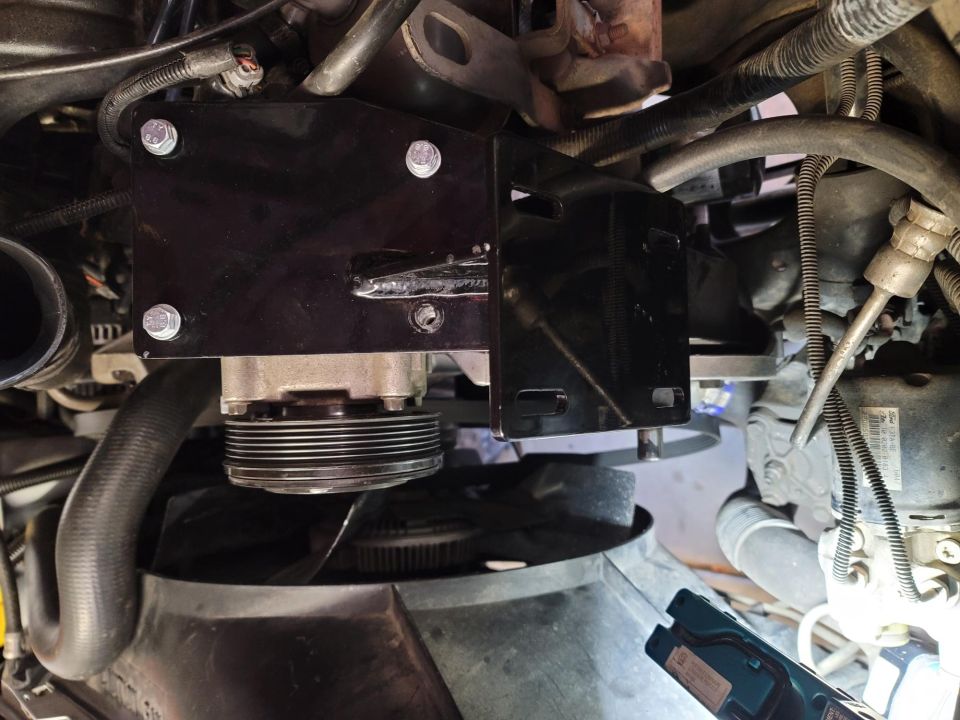 Black metal bracket installed on a 1996 Ford Bronco engine, holding a pulley.