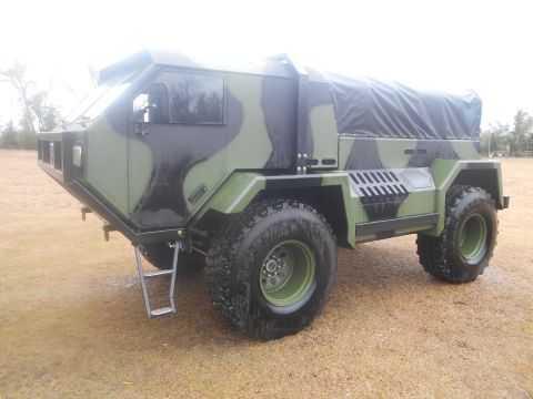 1992 Ford Bronco - A custom camouflage-painted, four-wheel-drive vehicle with a black canvas top sits parked on a grassy field. The vehicle has large, rugged…