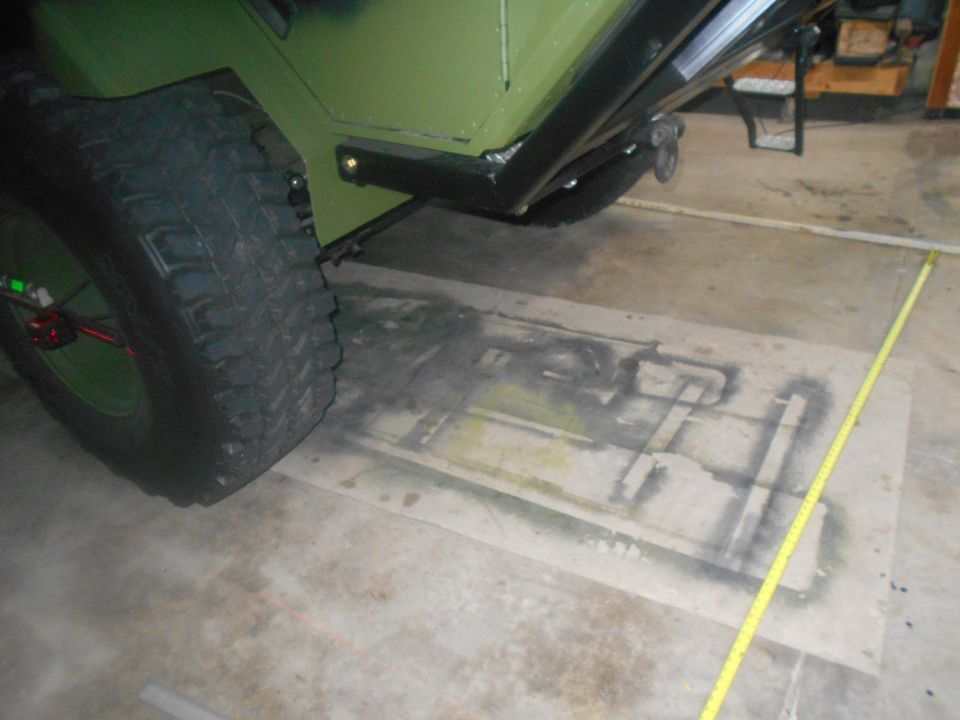 Green vehicle rear tire and fender with a yellow measuring tape on the ground.