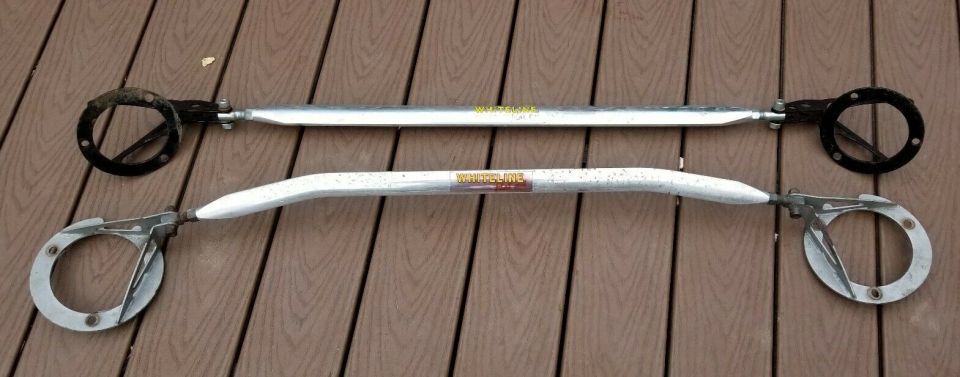 Two silver strut bars with black and silver mounting hardware on a wooden surface