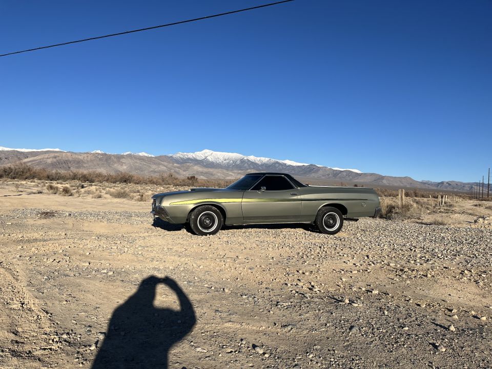 Side view of a 1972 Ford Ranchero parked on a dirt lot with mountains in the background