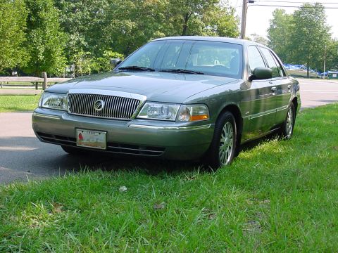 2003 Mercury Grand Marquis - A green 2003 Mercury Grand Marquis is parked on a grassy area with trees in the background.