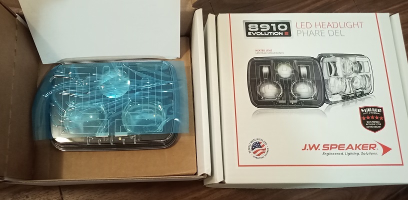 JW Speaker 8910 Evolution 2 LED headlight in box next to shipping box.