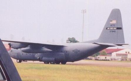1988 Ford Bronco - A gray military cargo airplane is parked on a tarmac with buildings in the background.
