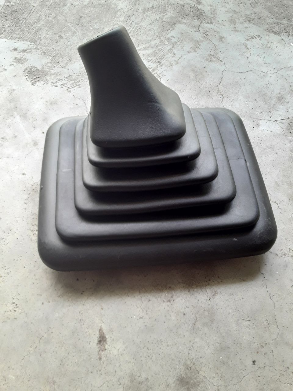 Black rubber shift boot with pleats on a concrete surface.