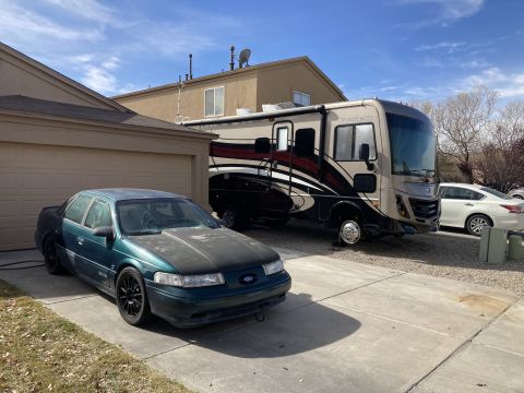 2015 Ford F-550 - A dark green sedan with a matte black hood sits parked on a concrete driveway next to a large RV. The sedan's windshield is cracked, and it…