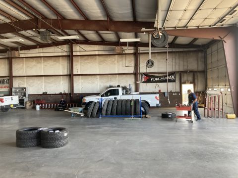 2015 Ford F-550 - A white Ford F-550 pickup truck is parked inside a garage with several tires stacked nearby. A mechanic in blue overalls is working on a ti…