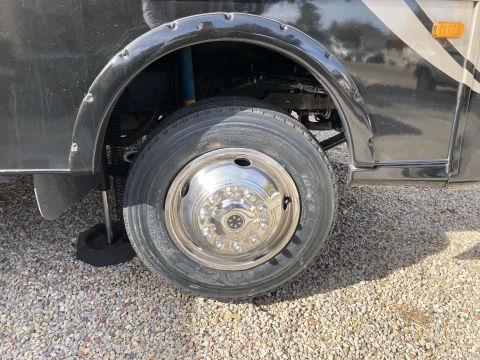 2015 Ford F-550 - Close-up view of the front passenger side wheel and fender well of a dark-colored RV. A chrome hubcap with a star emblem is visible on the…