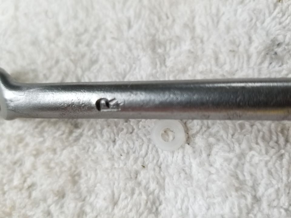 Metal tool with an R stamp and a white washer on a textured surface.