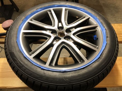 2019 Ford Everest - A close-up view of a silver alloy wheel with blue painter's tape applied to the rim, ready for detailing or painting. The wheel is mounted…