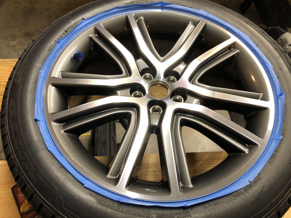 Gray multi-spoke car wheel with blue painter's tape on the rim, attached to a tire.