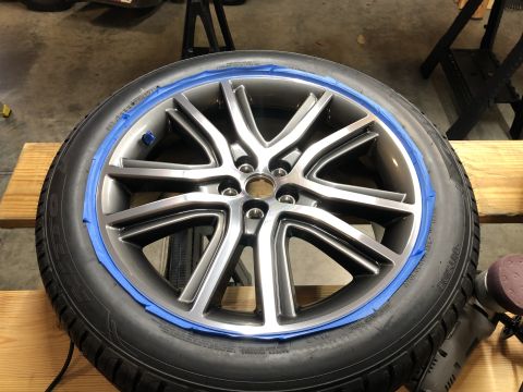 2019 Ford Everest - A close-up view shows a vehicle wheel and tire assembly with blue painter's tape applied around the rim. A rotary sander is visible on the…