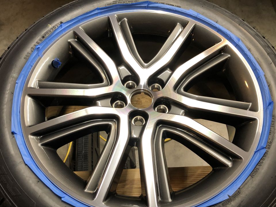 Gray multi-spoke alloy wheel with blue tape on tire edge.