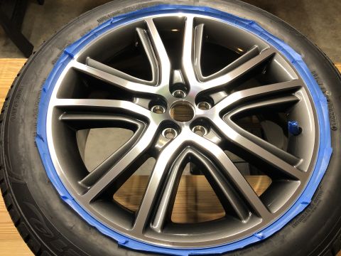 2019 Ford Everest - A close-up view of a gray alloy wheel with blue painter's tape applied around the rim, ready for detailing or painting. The tire is visible…