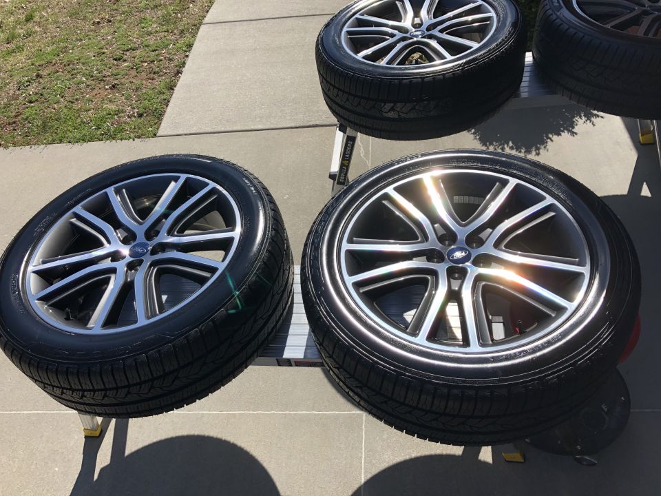 Four clean aftermarket wheels with silver and black spokes and blue Ford emblems.