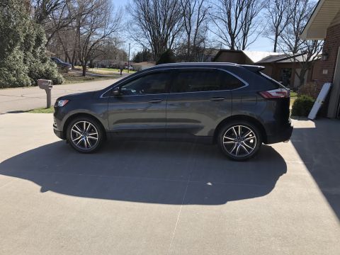 2019 Ford Everest - A dark gray Ford SUV is parked on a concrete driveway in front of a brick house. The vehicle is shown from the side profile, with its front…