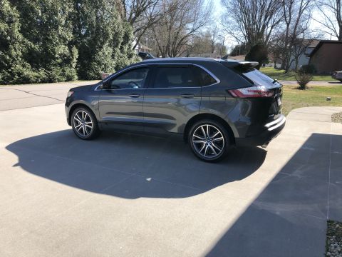 2019 Ford Everest - A dark gray Ford SUV is parked on a concrete driveway on a sunny day. The vehicle is viewed from the side, showing its sleek design and all…