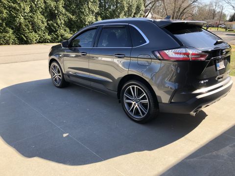 2019 Ford Everest - The rear passenger side of a dark gray SUV is shown parked on a concrete driveway. The vehicle has tinted windows and chrome accents around…