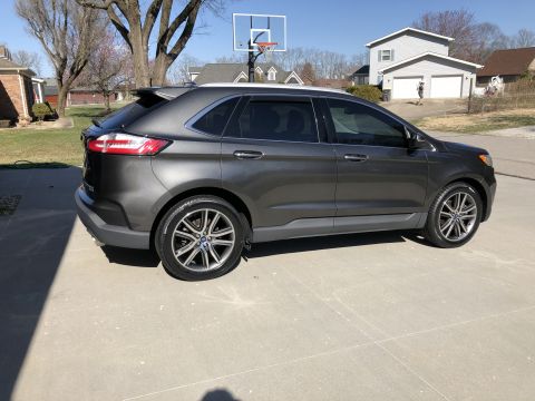 2019 Ford Everest - The side profile of a dark gray Ford Edge SUV is parked on a concrete driveway on a sunny day. The vehicle has tinted windows and aftermark…