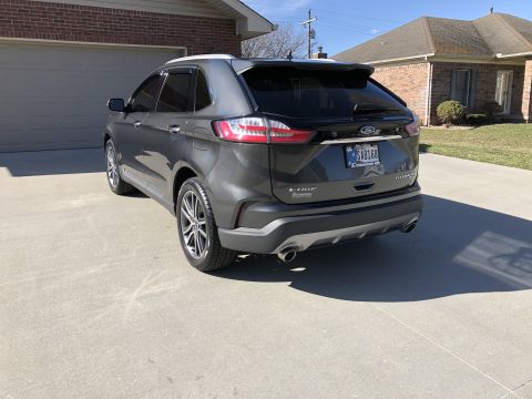 2019 Ford Everest - The rear of a 2019 Ford Edge Titanium SUV is shown parked in a driveway. The vehicle features polished wheels and a dark gray exterior.