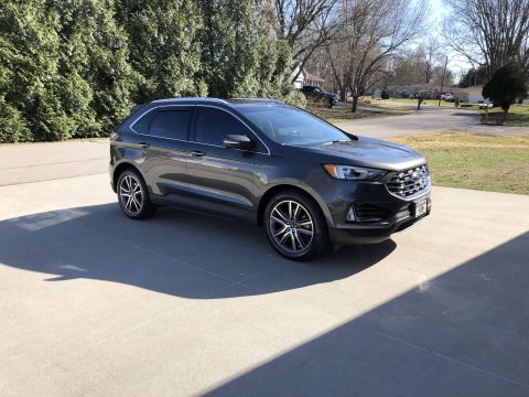 2019 Ford Everest - This dark gray SUV, likely a 2019 Ford Edge, is shown from a 3/4 front angle on a paved driveway with a backdrop of trees and houses.