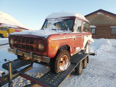 1996 Ford Bronco - Red Ford Bronco on a trailer, covered in snow, with a wooden building in the background.