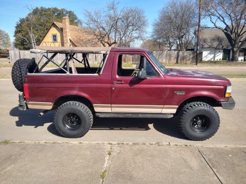 1996 Ford Bronco - Side view of a maroon 1996 Ford Bronco, a removable soft top and a spare tire mounted on the rear.