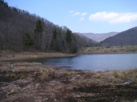 1994 Ford Bronco - A calm lake sits at the base of a wooded mountain range, with a concrete dam visible in the distance.