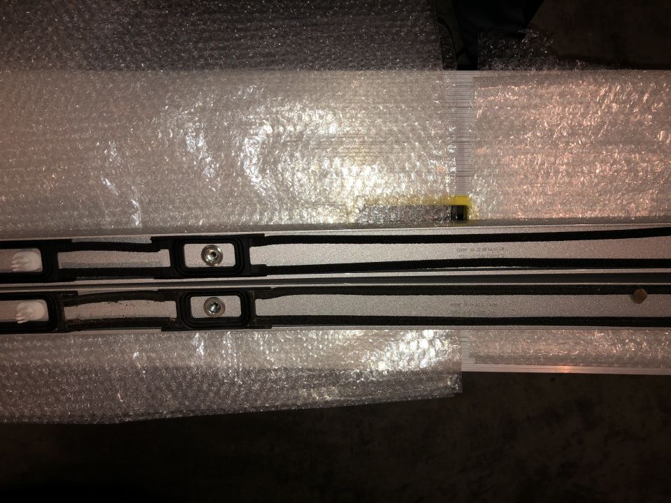 Close-up of two silver roof rack rails with black rubber seals and mounting points, wrapped in bubble wrap